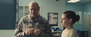 Movie still from “Camp X-Ray” (2014), directed by Peter Sattler – A man in a military fatigues and a woman in military fatigues are in a hospital room; Medium shot, Over the shoulder angle