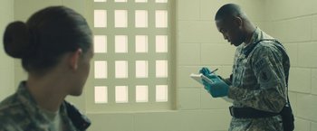 Movie still from “Camp X-Ray” (2014), directed by Peter Sattler – A person in a room with a cell phone; Medium shot, Over the shoulder angle