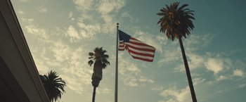 Movie still from “Camp X-Ray” (2014), directed by Peter Sattler – An american flag flying on top of a flag pole next to palm trees; Extreme Wide shot, Low angle