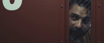 Movie still from “Camp X-Ray” (2014), directed by Peter Sattler – A man looking through a chain link fence; Close Up shot, Low angle