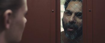 Movie still from “Camp X-Ray” (2014), directed by Peter Sattler – A man with a gray beard is looking through a fence; Close Up shot, Over the shoulder angle