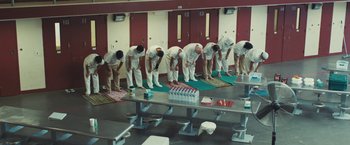Movie still from “Camp X-Ray” (2014), directed by Peter Sattler – A group of men standing in a room with their feet on the ground; Wide shot, High angle