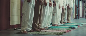 Movie still from “Camp X-Ray” (2014), directed by Peter Sattler – A group of people standing on top of a rug; Wide shot, Overhead angle