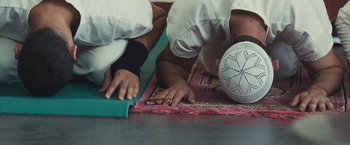 Movie still from “Camp X-Ray” (2014), directed by Peter Sattler – Two men kneeling on the ground in prayer; Extreme Close Up shot, Overhead angle
