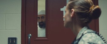 Movie still from “Camp X-Ray” (2014), directed by Peter Sattler – A man with a beard looking at a woman through a window; Close Up shot, Over the shoulder angle