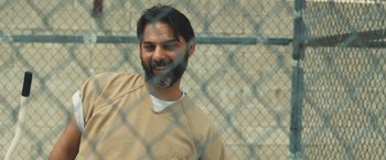 Movie still from “Camp X-Ray” (2014), directed by Peter Sattler – A man with a beard is standing in front of a chain link fence; Close Up shot, Over the shoulder angle
