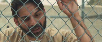 Movie still from “Camp X-Ray” (2014), directed by Peter Sattler – A man with a beard is behind a chain link fence; Close Up shot, Over the shoulder angle