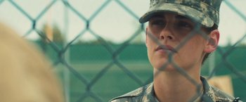 Movie still from “Camp X-Ray” (2014), directed by Peter Sattler – A woman in fatigues is looking through a chain link fence; Close Up shot, Low angle