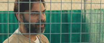 Movie still from “Camp X-Ray” (2014), directed by Peter Sattler – A man with a goatee looking out of a cage; Close Up shot, Over the shoulder angle
