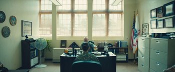 Movie still from “Camp X-Ray” (2014), directed by Peter Sattler – A man sitting at a desk in front of another man; Wide shot, Over the shoulder angle