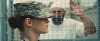 Movie still from “Camp X-Ray” (2014), directed by Peter Sattler – A man in a military uniform and a woman in fatigues look at each other through a fence; Medium shot, Over the shoulder angle
