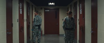 Movie still from “Camp X-Ray” (2014), directed by Peter Sattler – A couple of men standing next to each other in front of a door; Wide shot, Over the shoulder angle