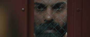 Movie still from “Camp X-Ray” (2014), directed by Peter Sattler – A person with a beard behind a fence; Extreme Close Up shot, Overhead angle