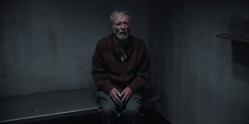 Movie still from “Dark” (2017), created by Baran bo Odar – An older man sitting on a bench in a dark room; Medium shot, High angle