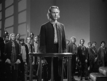 Movie still from “Captain Blood” (1935), directed by Michael Curtiz – A black and white photo of a man standing in front of a group of people; Medium shot, Low angle