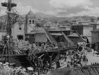 Movie still from “Captain Blood” (1935), directed by Michael Curtiz – A black and white photo of a boat in a harbor; Extreme Wide shot, High angle