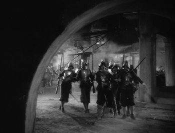 Movie still from “Captain Blood” (1935), directed by Michael Curtiz – A black and white photo of a group of men in medieval garb; Extreme Wide shot, High angle