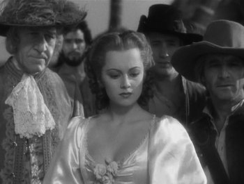 Movie still from “Captain Blood” (1935), directed by Michael Curtiz – A black and white photo of a woman in a dress; Medium shot, Over the shoulder angle