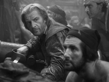 Movie still from “Captain Blood” (1935), directed by Michael Curtiz – A black and white photo of a man sitting on a motorcycle; Medium shot, Over the shoulder angle