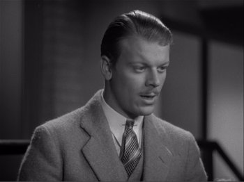 Movie still from “Captains Courageous” (1937), directed by Victor Fleming – A man wearing a suit and tie in front of a brick wall; Close Up shot, High angle