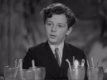Movie still from “Captains Courageous” (1937), directed by Victor Fleming – A young man in a suit and tie sitting in front of a bunch of cups; Close Up shot, High angle