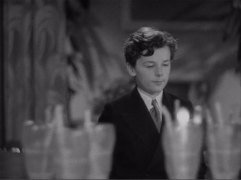 Movie still from “Captains Courageous” (1937), directed by Victor Fleming – A young man in a suit and tie in front of a row of cups; Close Up shot, High angle