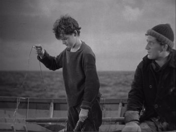 Movie still from “Captains Courageous” (1937), directed by Victor Fleming – A young boy holding a fishing pole next to another young man; Medium shot, High angle