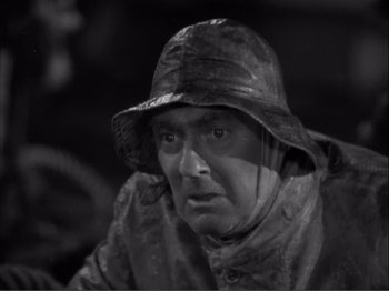 Movie still from “Captains Courageous” (1937), directed by Victor Fleming – A black and white photo of a man wearing a rain coat and hat; Close Up shot, High angle