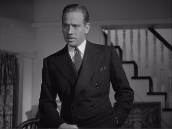 Movie still from “Captains Courageous” (1937), directed by Victor Fleming – A man in a suit and tie standing next to a chair; Close Up shot, Low angle