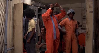 Movie still from “Car Wash” (1976), directed by Michael Schultz – A group of men in orange jumpsuits in a locker room; Medium shot, Low angle