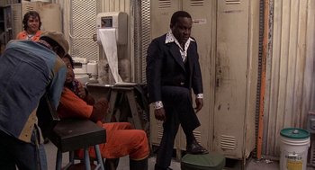 Movie still from “Car Wash” (1976), directed by Michael Schultz – A man in a suit and tie standing next to a person in an orange suit; Medium shot, Low angle