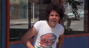 Movie still from “Car Wash” (1976), directed by Michael Schultz – A young man with curly hair and a t - shirt with an image of a man's face on it; Close Up shot, Low angle