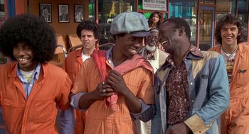 Movie still from “Car Wash” (1976), directed by Michael Schultz – A group of men standing next to each other on a street; Medium shot, Over the shoulder angle