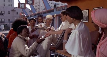 Movie still from “Car Wash” (1976), directed by Michael Schultz – A group of people sitting around each other on a bench; Medium shot, High angle