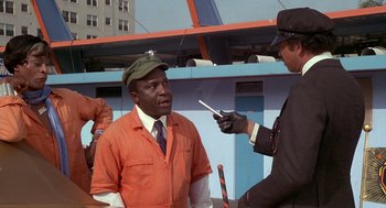 Movie still from “Car Wash” (1976), directed by Michael Schultz – A man in an orange jumpsuit is being interviewed by a man in an orange suit; Medium shot, Over the shoulder angle