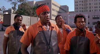 Movie still from “Car Wash” (1976), directed by Michael Schultz – A group of men in orange shirts and aprons standing next to each other on a street; Medium shot, Low angle