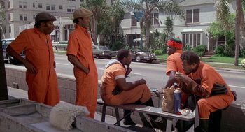 Movie still from “Car Wash” (1976), directed by Michael Schultz – A group of men sitting on top of a wooden bench; Wide shot, Low angle