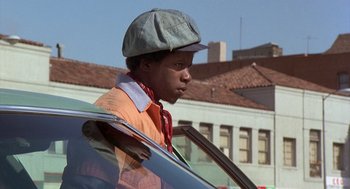 Movie still from “Car Wash” (1976), directed by Michael Schultz – A young man in an orange shirt and hat is looking out of a car window; Close Up shot, Low angle