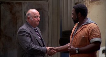 Movie still from “Car Wash” (1976), directed by Michael Schultz – Two men shaking hands in front of a building; Medium shot, Over the shoulder angle