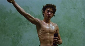 Movie still from “Caravaggio” (1986), directed by Derek Jarman – A shirtless man holding a cell phone in his hand; Medium shot, Low angle