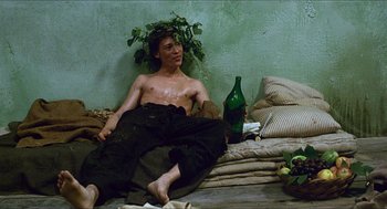 Movie still from “Caravaggio” (1986), directed by Derek Jarman – A shirtless man sitting on a bed next to a bottle of wine; Medium shot, Low angle