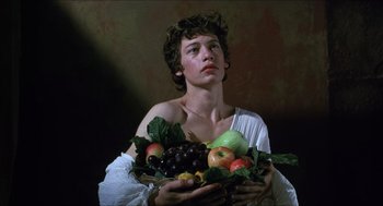Movie still from “Caravaggio” (1986), directed by Derek Jarman – A young man holding a basket of fruit in his hands; Medium shot, Low angle