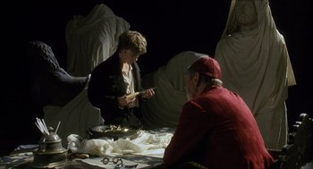 Movie still from “Caravaggio” (1986), directed by Derek Jarman – Two people sitting at a table with a pan of food on it; Medium shot, Over the shoulder angle