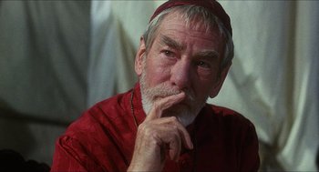 Movie still from “Caravaggio” (1986), directed by Derek Jarman – An older man in a red shirt is sitting with his hand under his chin; Close Up shot, Low angle