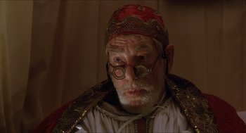 Movie still from “Caravaggio” (1986), directed by Derek Jarman – An old man with a beard wearing a red hat and glasses; Close Up shot, Over the shoulder angle