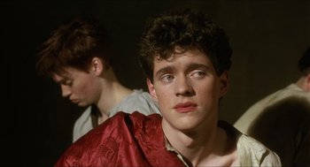 Movie still from “Caravaggio” (1986), directed by Derek Jarman – A young man in a red robe looking at the camera; Close Up shot, Over the shoulder angle