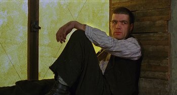 Movie still from “Caravaggio” (1986), directed by Derek Jarman – A man sitting on the ground with his legs crossed; Medium shot, Low angle