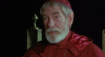 Movie still from “Caravaggio” (1986), directed by Derek Jarman – An older man with a beard wearing a red robe; Close Up shot, Over the shoulder angle