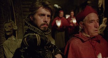 Movie still from “Caravaggio” (1986), directed by Derek Jarman – A man with a beard is wearing a black and red outfit; Close Up shot, Over the shoulder angle