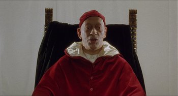 Movie still from “Caravaggio” (1986), directed by Derek Jarman – An older man wearing a red robe sitting in a chair; Close Up shot, High angle